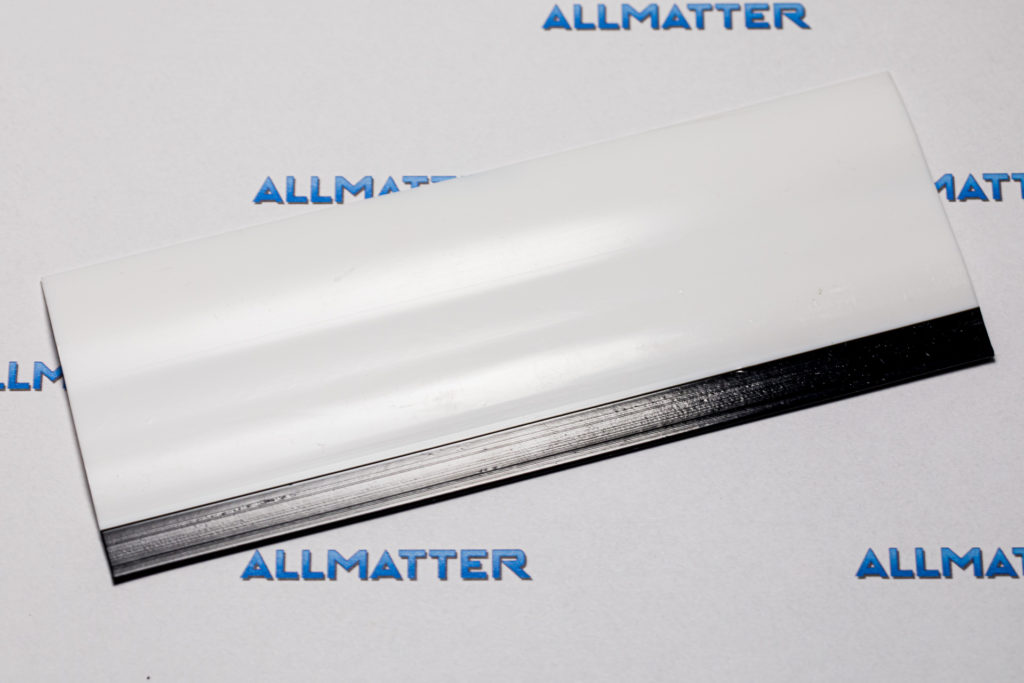 Biała szpachelka z czarnym brzegiem na tle z logo Allmatter